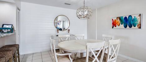 A dining area with a round table, white chairs, and a hanging light fixture.