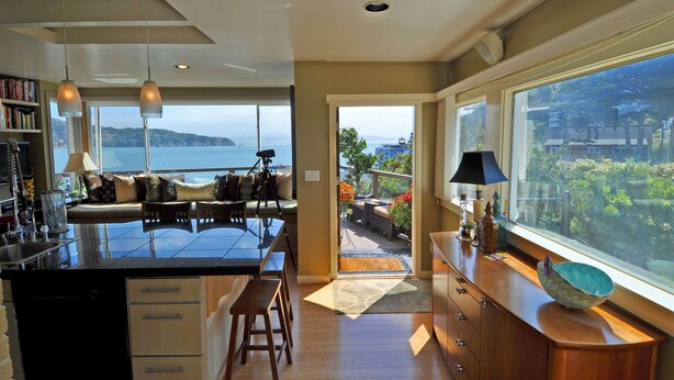 A modern kitchen with a large island, a dining area with a view, and a spacious living area with a balcony overlooking the sea.