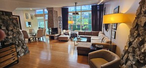 A spacious living room with a fireplace, a sofa, a coffee table, and a dining area with chairs. - Luxury 2BR with Pool & Panoramic Golden Gate  and Skyline Views (Tiburon)
