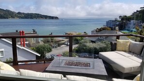 Un balcón con sofá y una chimenea, con vistas a la costa, edificios y el mar.