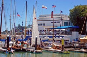 A marina with multiple boats docked, a building with a sign that reads 'Yacht Club', and people on the dock. - Luxury 2BR with Pool & Panoramic Golden Gate  and Skyline Views (Tiburon)