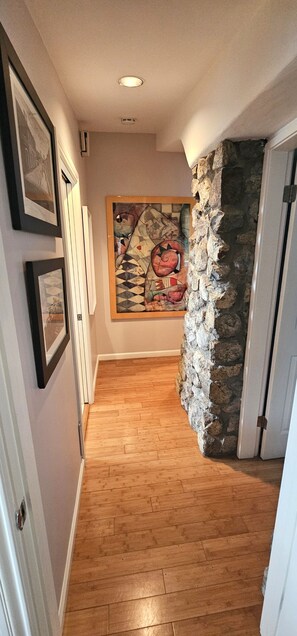 A hallway with wooden flooring, a stone accent wall, and framed artwork on the walls. - Luxury 2BR with Pool & Panoramic Golden Gate  and Skyline Views (Tiburon)