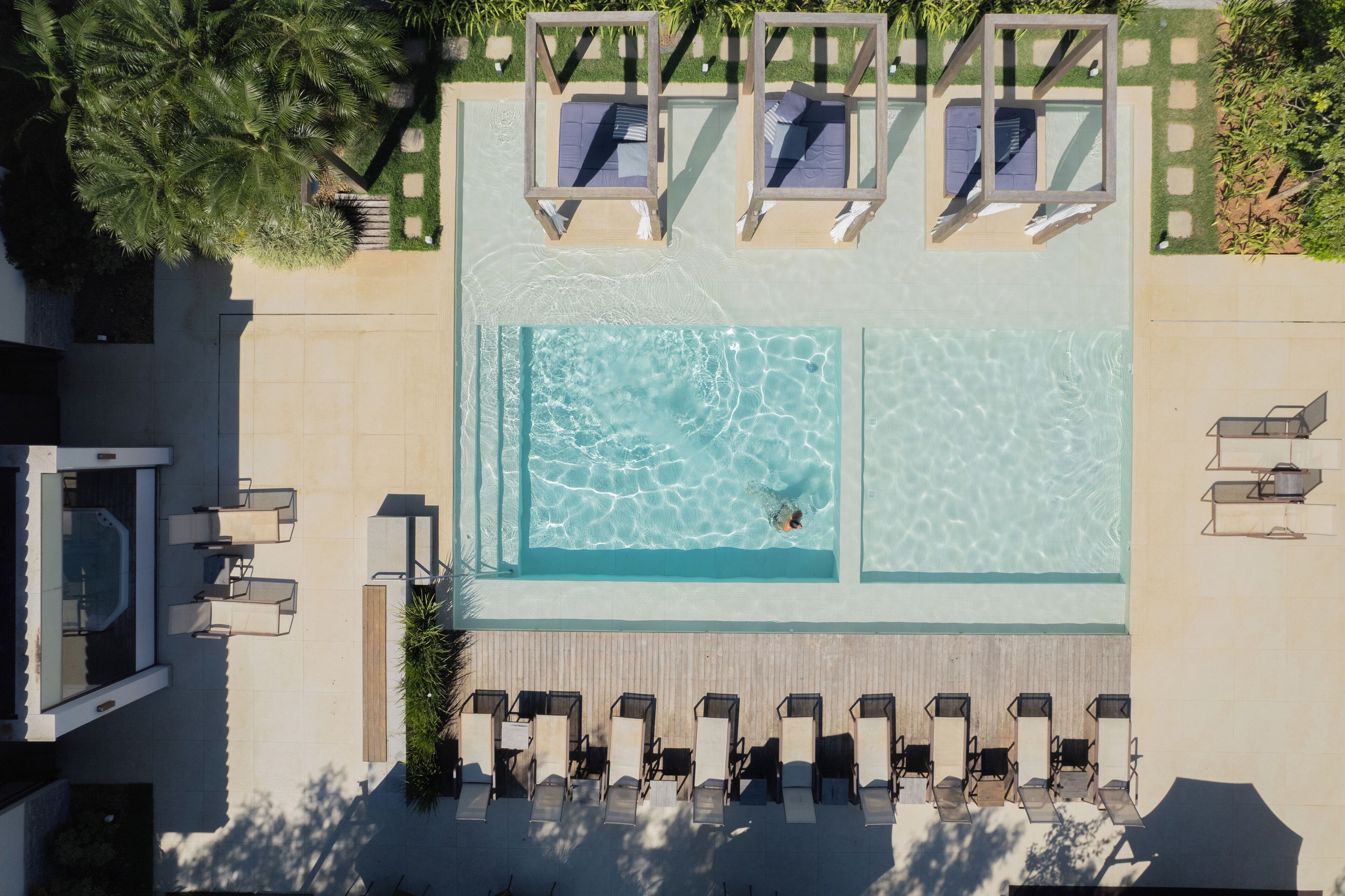 An aerial view of a swimming pool with lounge chairs and a hot tub area.