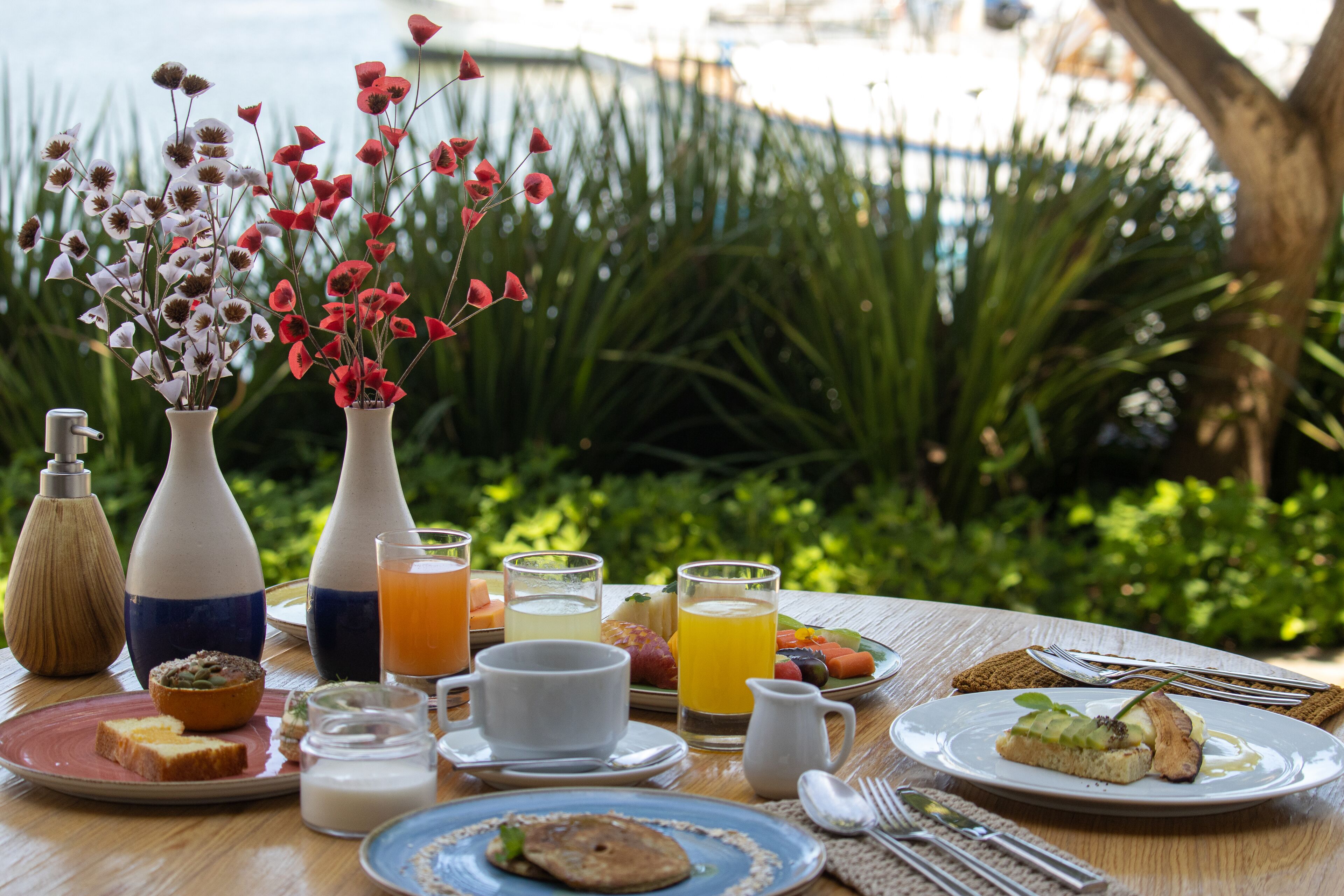 A breakfast table with various food items, drinks, and a vase of flowers.