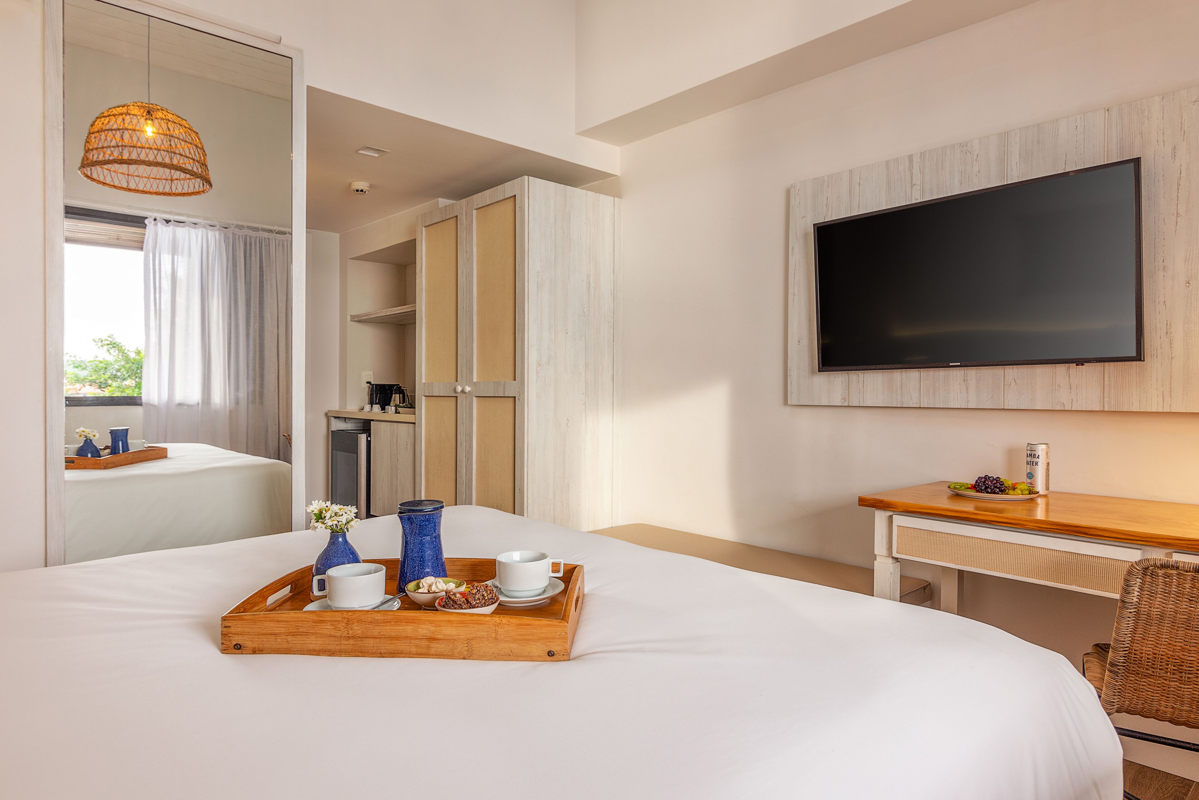 Habitación de hotel con cama, mesita de noche de madera, televisor y bandeja de desayuno con taza, plato y florero.