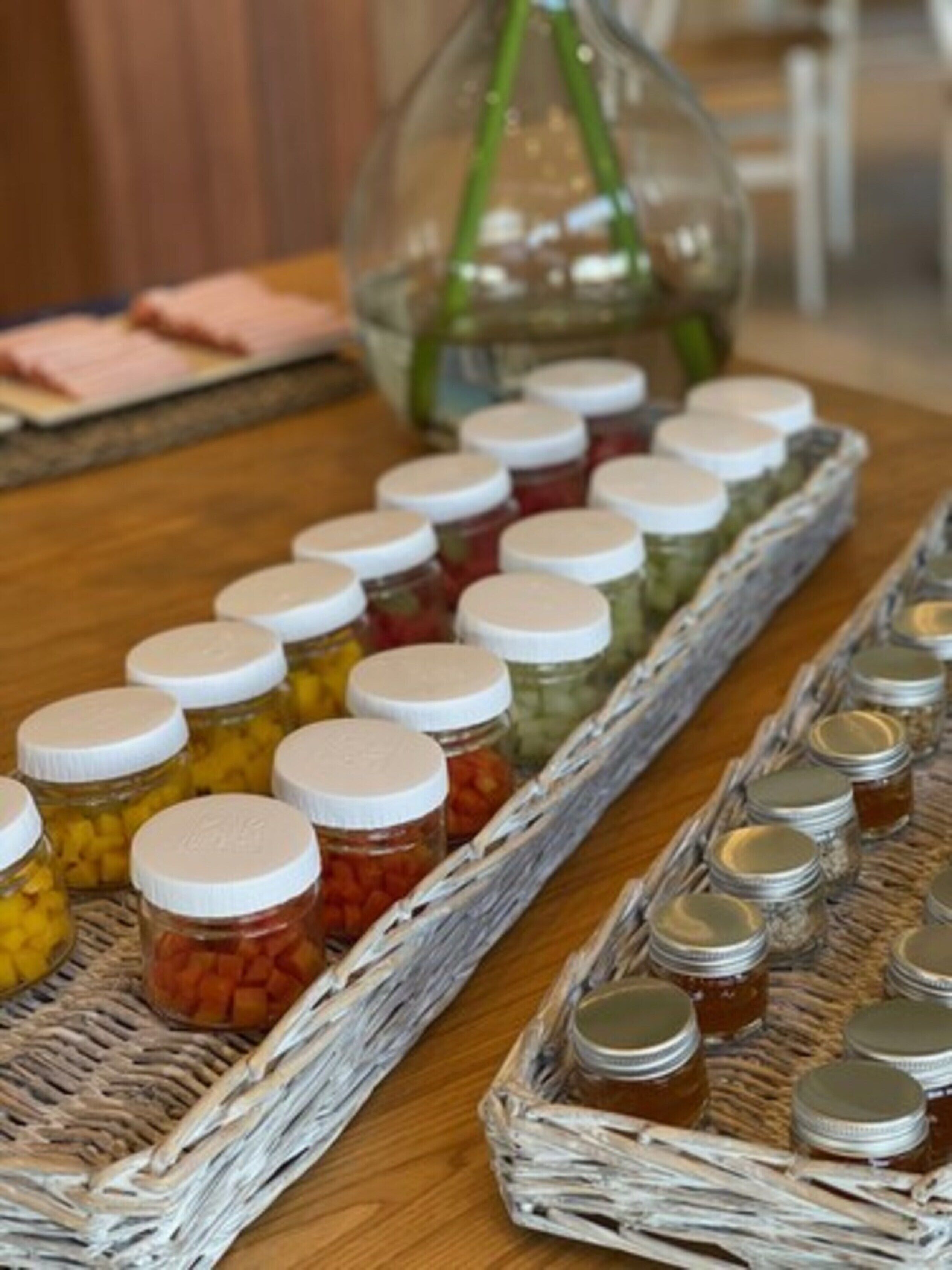 Una mesa con frascos de verduras encurtidas en cestas de mimbre.