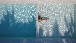 An aerial view of a swimming pool with clear water and a person lying on the edge. - Hotel Aretê (Búzios)