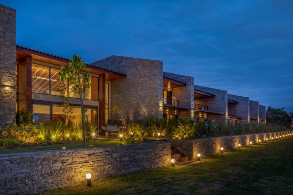 A modern building with large windows and stone walls, surrounded by a well-lit garden. - Hotel Aretê (Búzios)