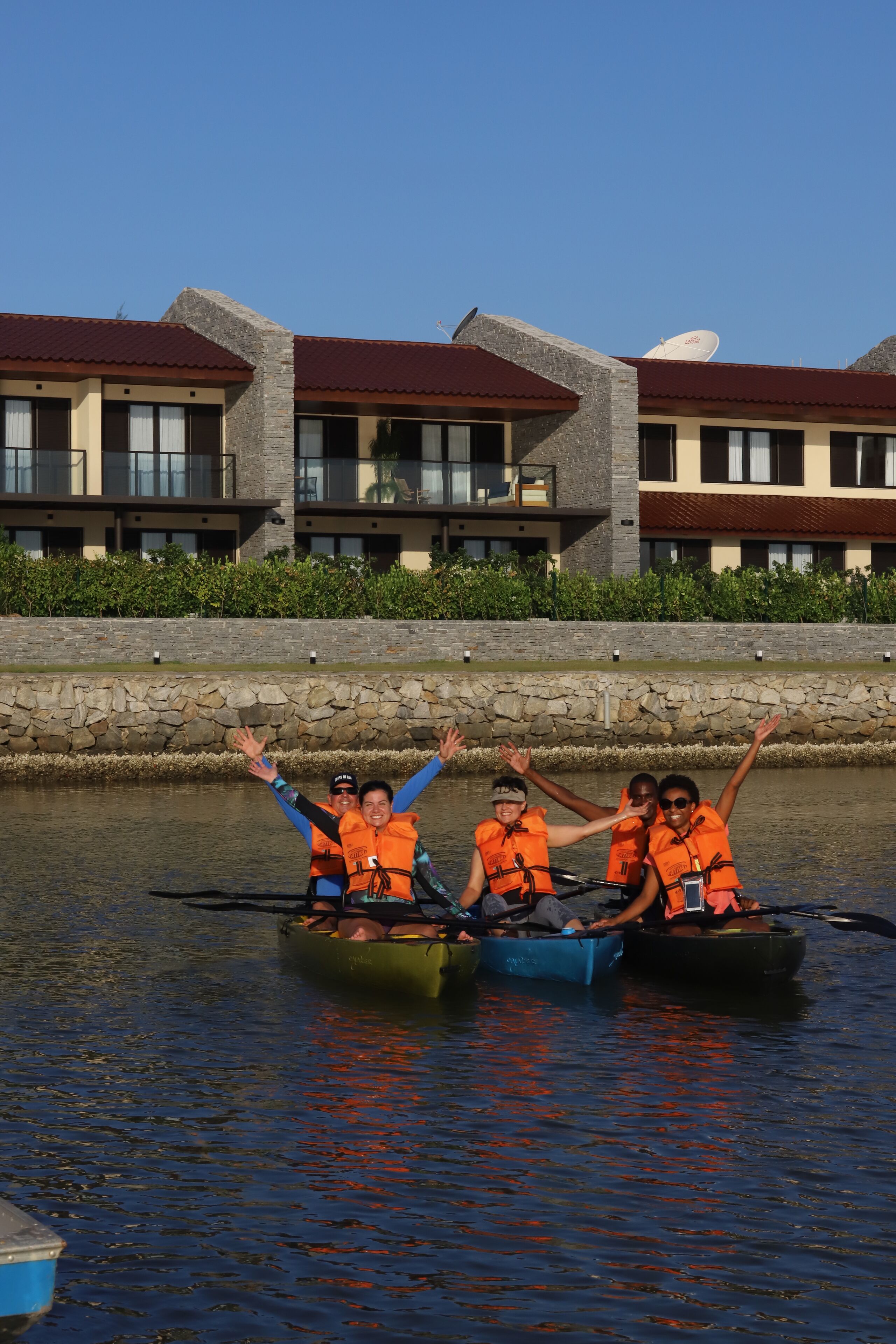 A group of people in canoes on a calm body of water, wearing orange life jackets.