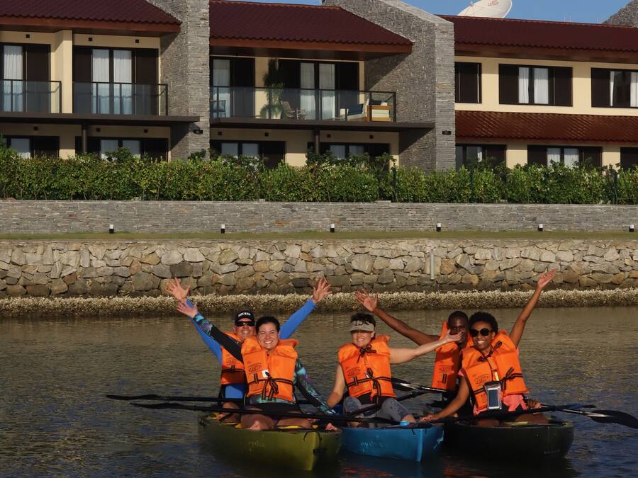A group of people in canoes on a calm body of water, wearing orange life jackets.