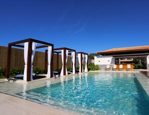A clear swimming pool with a wooden deck, a covered seating area, and a bar with outdoor seating. - Hotel Aretê (Búzios)