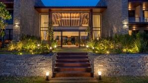 A modern building with a stone facade, large windows, and a well-lit entrance with steps leading up to it. - Hotel Aretê (Búzios)