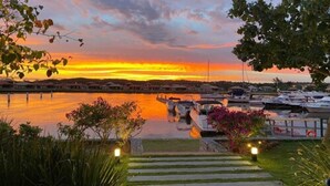 A marina with boats docked, a sunset in the background, and a pathway leading to the water. - Hotel Aretê (Búzios)