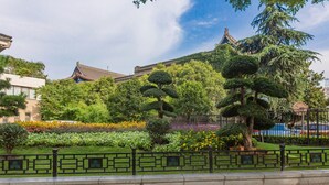 A landscaped garden with neatly trimmed trees and flower beds, a traditional building with a tiled roof, and a stone fence in the foreground. - Jinjiang Inn Select (Xi'an)
