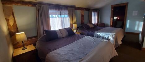 A hotel room with two beds, a nightstand with a lamp, and a window with curtains.