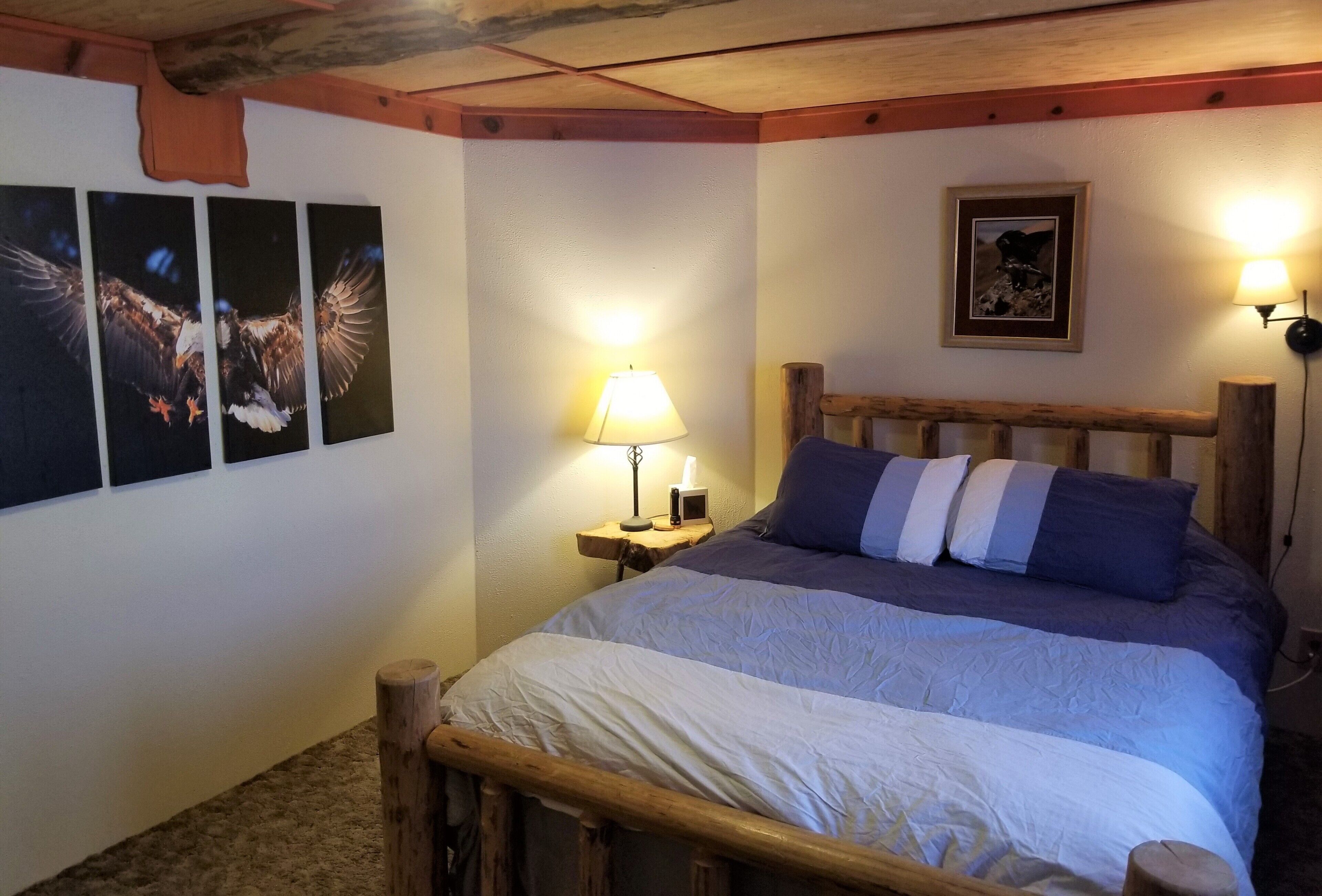 Makuuhuoneessa on puinen sänky, yöpöytä, jossa on lamppu, ja seinällä on kolme kehystettyä valokuvaa.