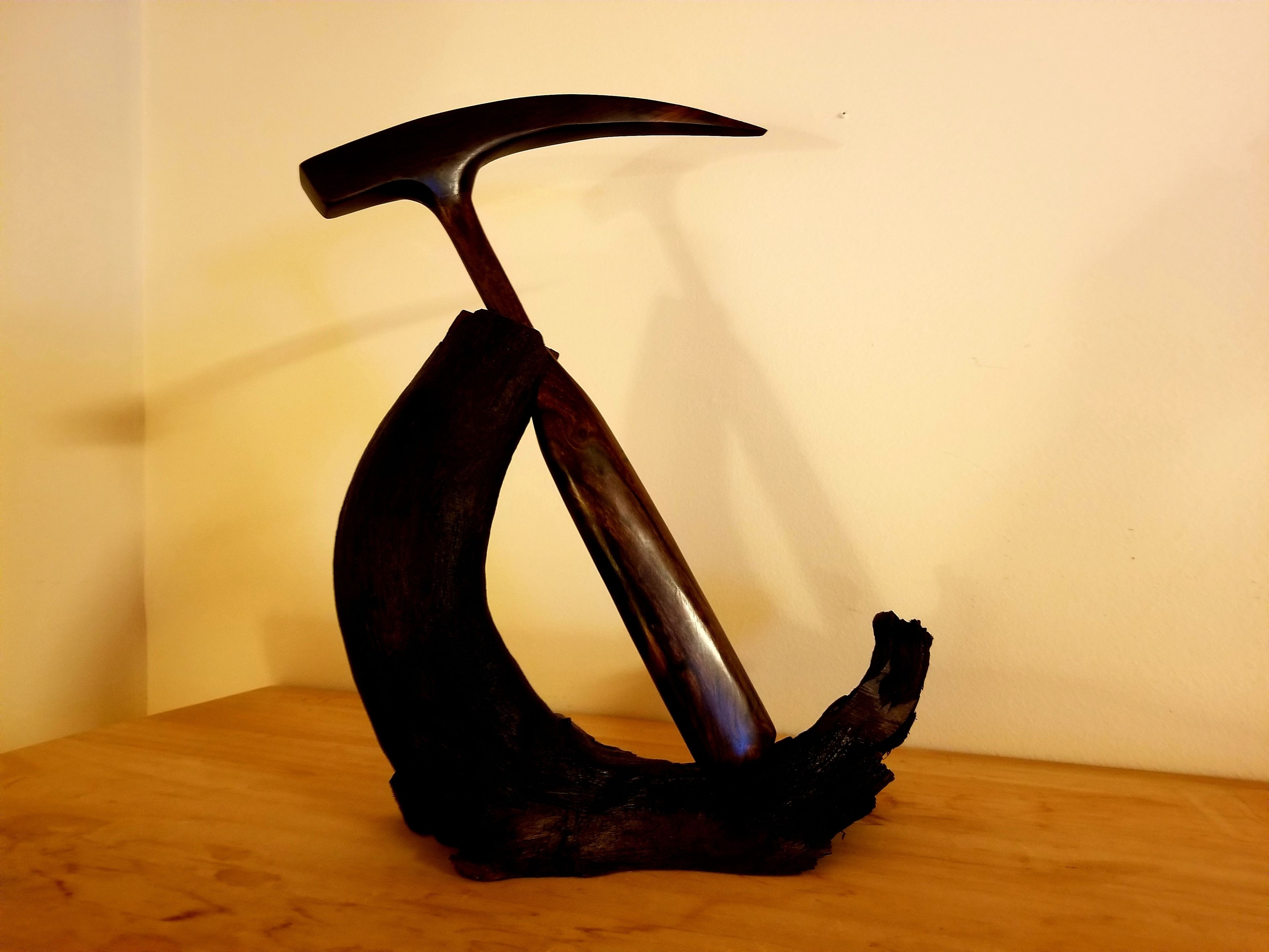 Une sculpture métallique représentant une pioche, montée sur un socle en bois.