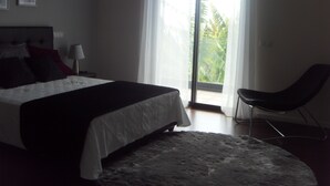 Ein Schlafzimmer mit einem Bett, einem Sessel, einer Lampe und Blick durch ein Fenster.