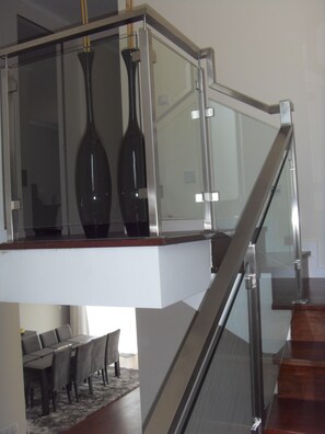 A modern interior with a glass railing, a dining area with a table and chairs, and two dark vases on a shelf.