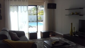 Ein Wohnzimmer mit Sofa, Hocker, Couchtisch, Fernseher und Blick auf einen Pool.