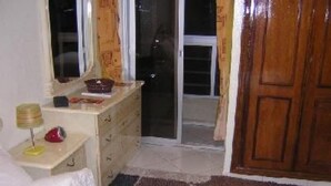 Een slaapkamer met een bed, nachtkastje met lamp, een dressoir en een schuifdeur naar een balkon.