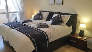 A double bed with a black and white bedspread, multiple pillows, and a bedside table with a lamp.