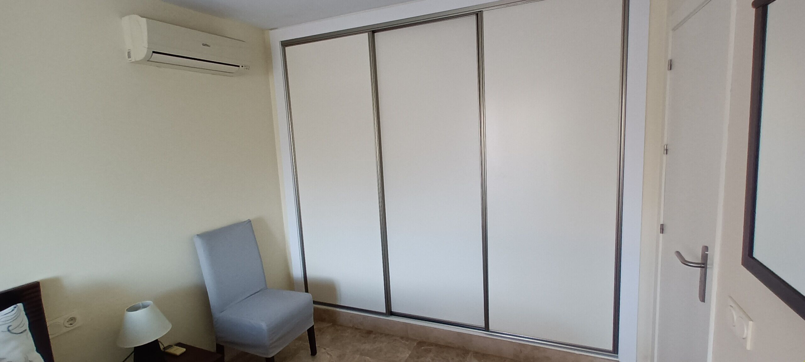 A room with a sliding door, a chair, a lamp, and an air conditioning unit.