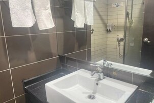 Un baño con lavamanos blanco, un espejo y zona de ducha.