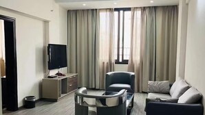 A modern living room with a sofa, armchair, TV, and a small table. - Cang Long Hotel (Hezhou)