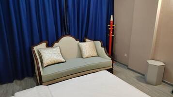Habitación de hotel con cama, sofá con cojines estampados, un lápiz rojo y un cesto de basura.