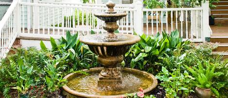 A garden with a stone fountain surrounded by lush greenery and a white fence.
