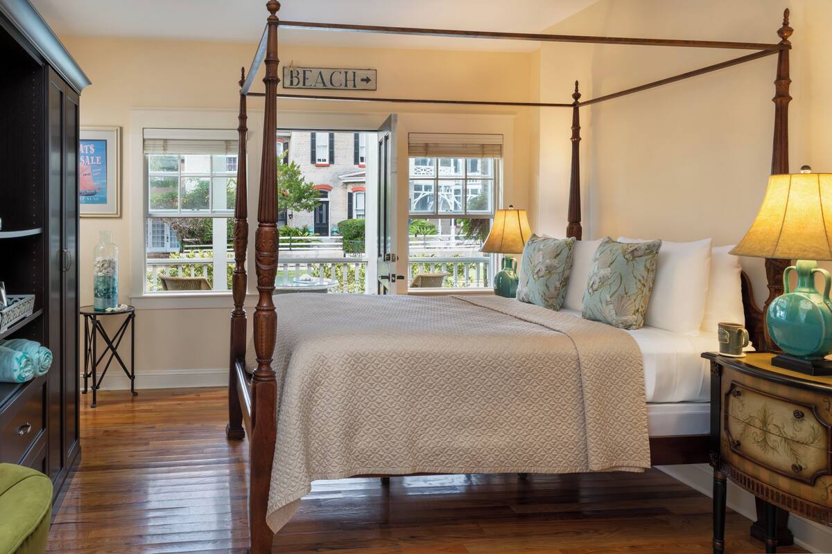 A four-poster bed with a view of the outside, a lamp, and a dresser.