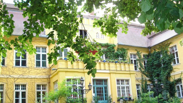 Ein gelbes Gebäude mit einer blauen Tür und Stufen, die davor hinaufführen, sowie ein Fahrrad, das davor abgestellt ist.