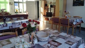 Un coin repas avec une table dressée pour deux personnes, un vase rempli de fleurs et un téléviseur en arrière-plan.