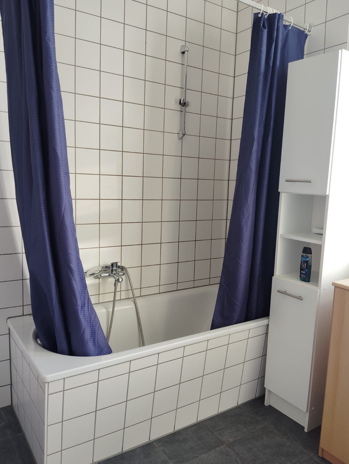 A bathroom with a bathtub, a shower, and a white cabinet with a bottle on the shelf.