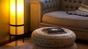 A room with a tall floor lamp, a tufted sofa, and a woven ottoman with a book.