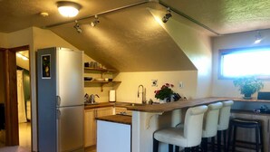A compact kitchen with a refrigerator, sink, and bar stools.