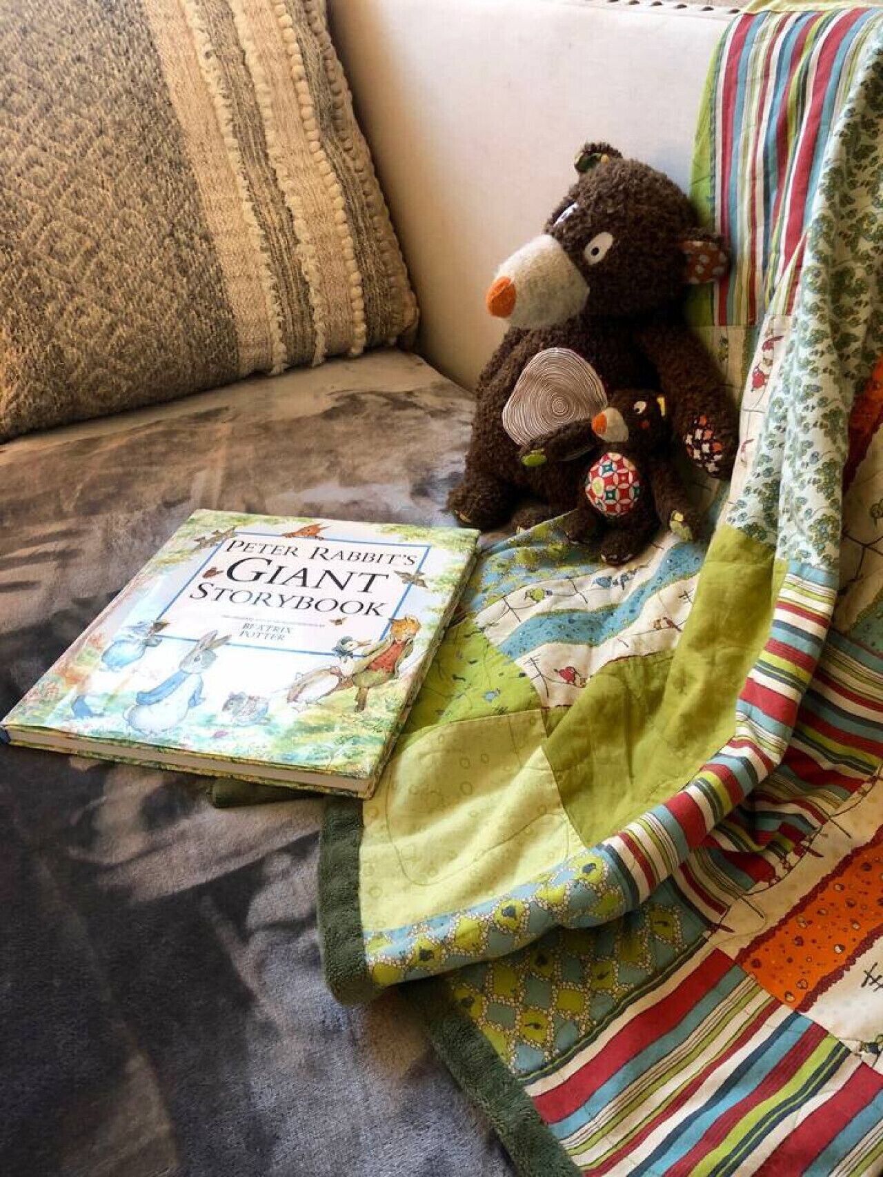 Ein Plüschtier, ein Buch mit dem Titel 'Peter Rabbit's Giant Storybook' und eine Steppdecke auf einer Couch.
