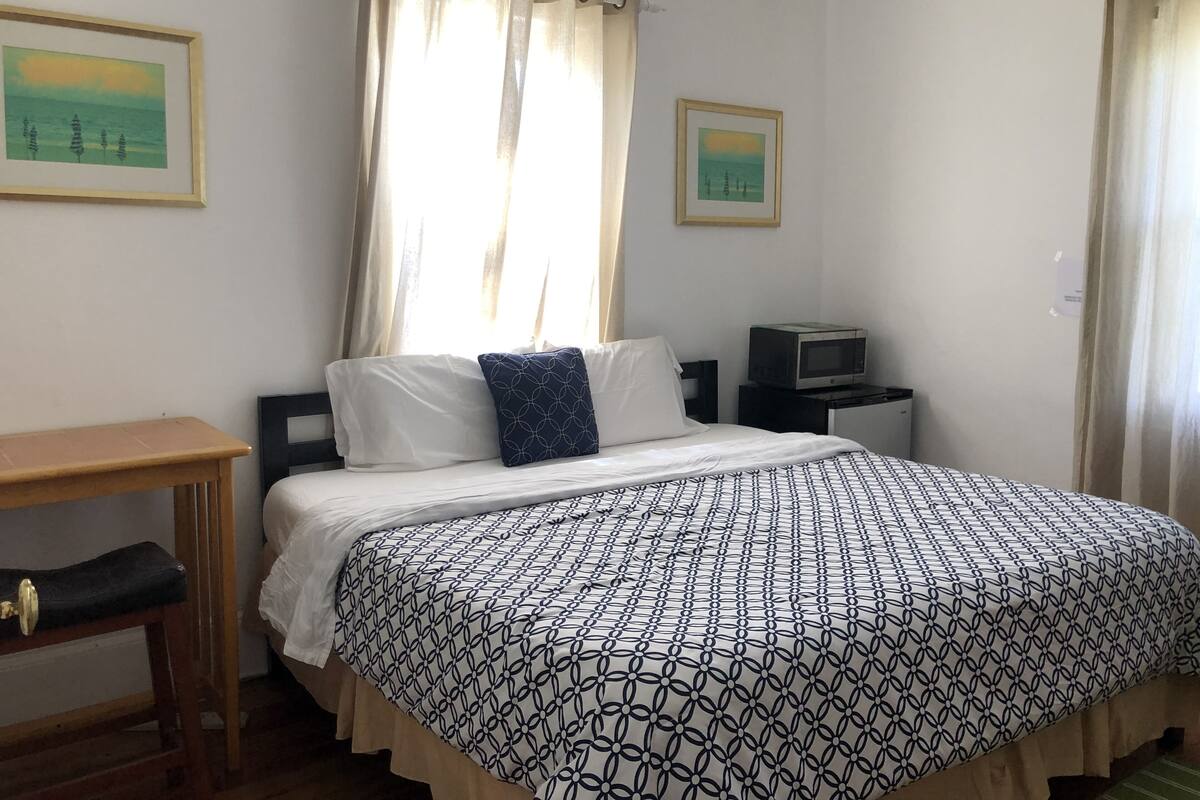 A bedroom with a bed, a desk, a chair, a television, and two framed pictures on the wall.