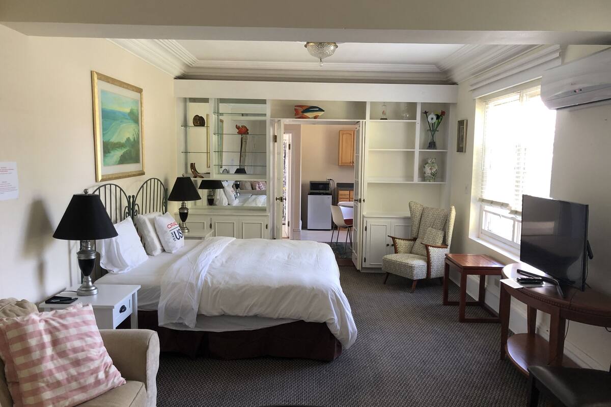 A hotel room with a bed, a desk, a chair, a television, and a window.