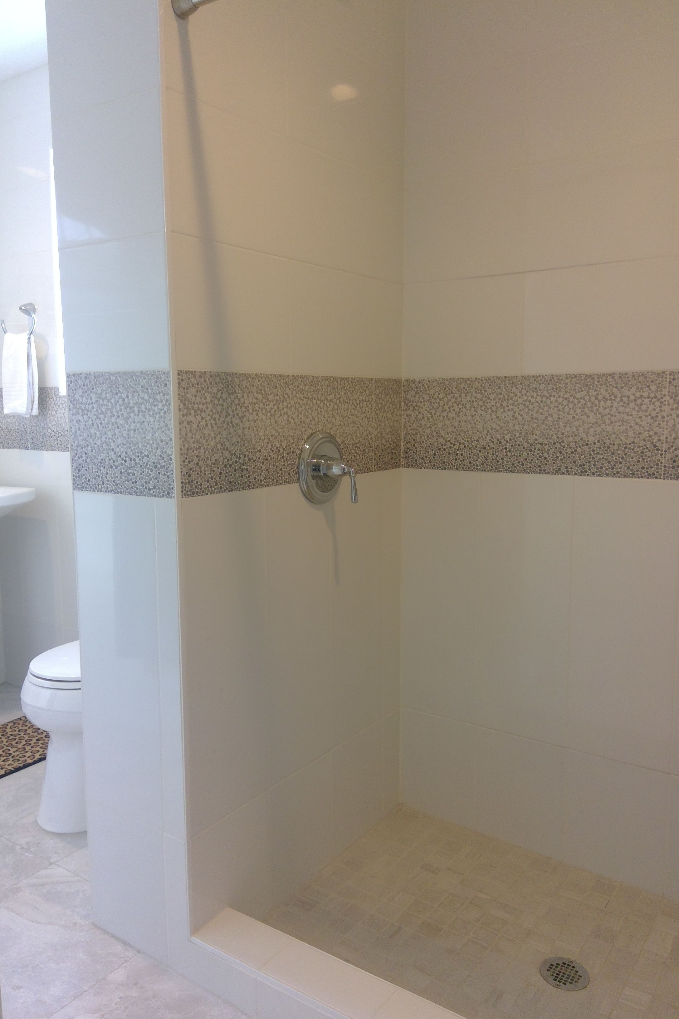 A shower area with a tiled wall, a drain, and a toilet visible in the background.