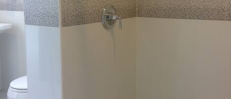 A shower area with a tiled wall, a drain, and a toilet visible in the background.