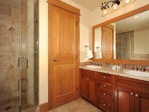 Une salle de bain avec deux lavabos, des meubles en bois, un grand miroir et une cabine de douche en verre.