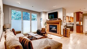 A spacious living room with a fireplace, a television, and a large window. - Fireplace & Private Balcony | Pool & Hot Tub (Edwards)