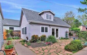 A single-story house with a front porch, a small garden with potted plants, and a paved driveway.