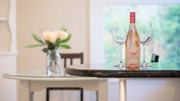 A table with a bottle of wine and two glasses on it, a vase with flowers, and a window in the background.