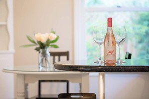 A table with a bottle of wine and two glasses on it, a vase with flowers, and a window in the background.