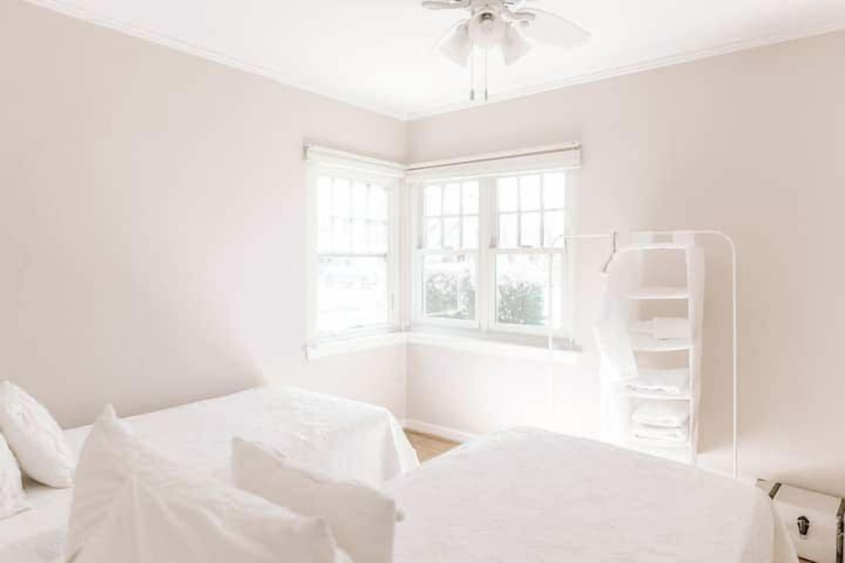 A room with two beds, a window, and a white shelving unit.