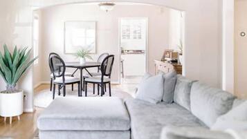 Una sala de estar con un sofá gris, una mesa de comedor con sillas y una planta en maceta.