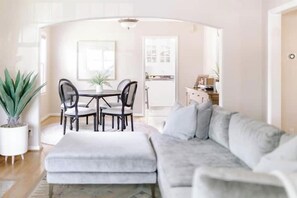 A living room with a grey sofa, a dining table with chairs, and a potted plant.
